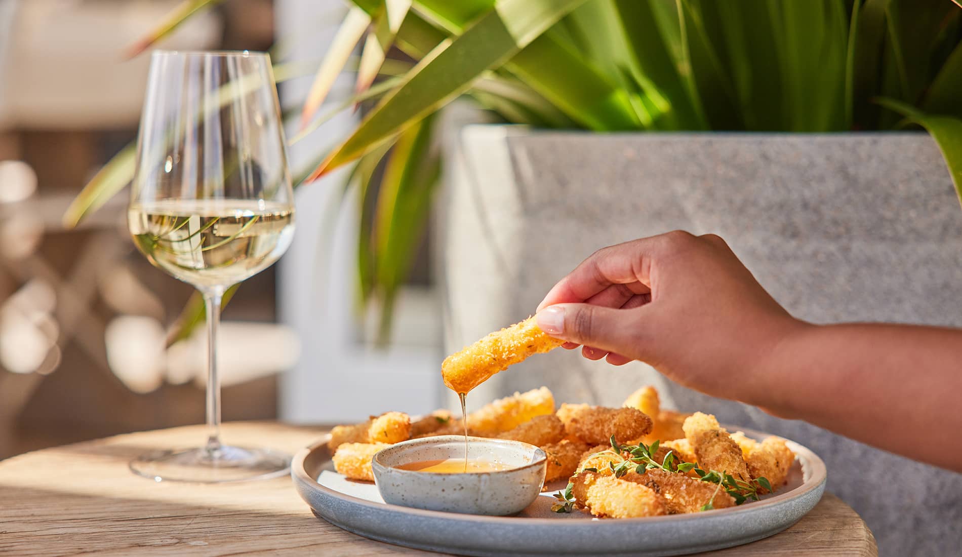 Hand holding croquette beside glass of white wine 